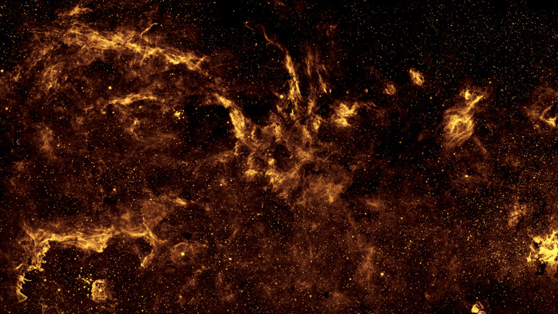 This infrared image of Milky Way galaxy looks like a splatter of gold paint and burgundy clouds on a black, star-studded canvass. 